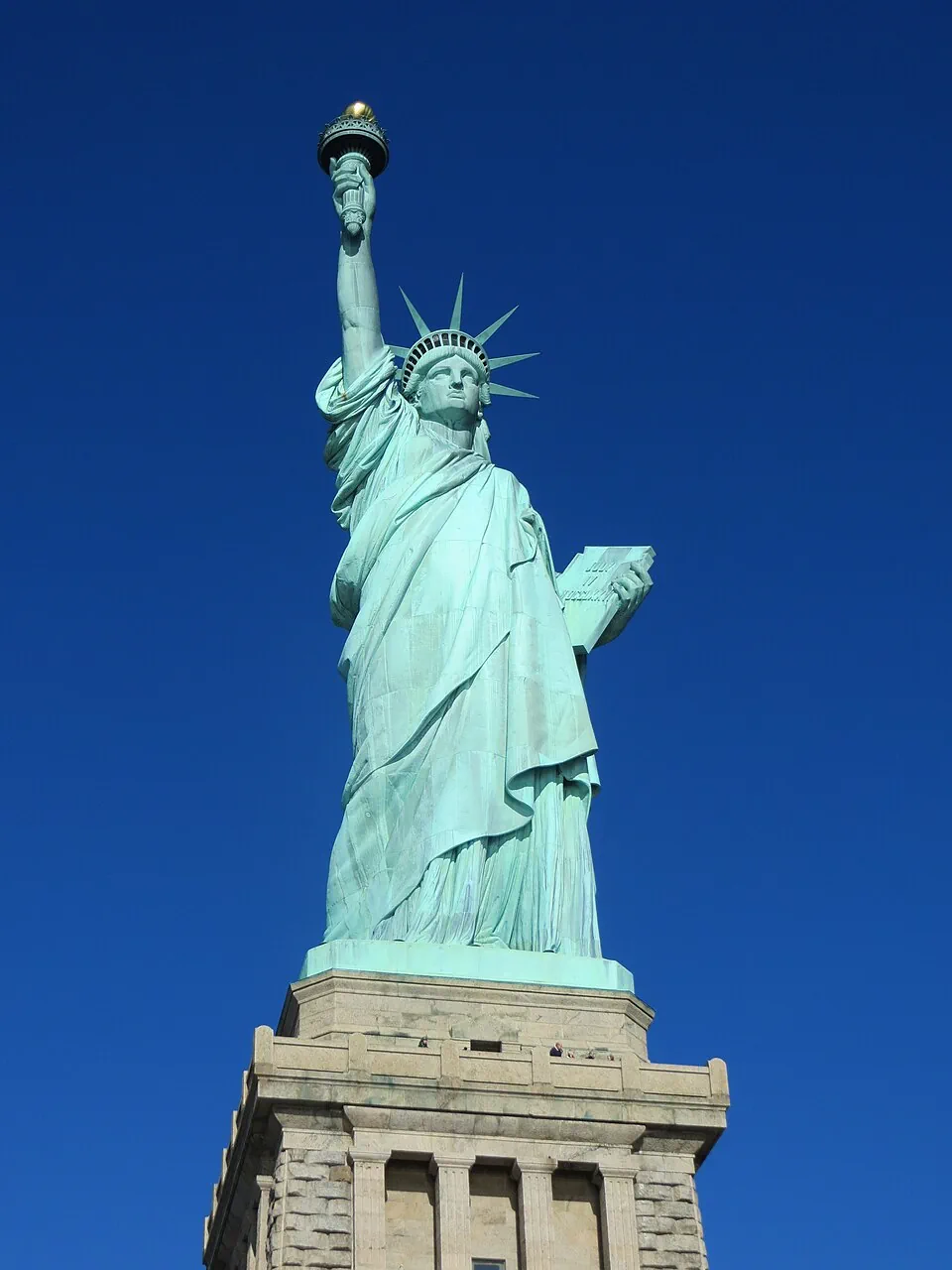 The Statue of Liberty, torch raised, against a clear blue sky